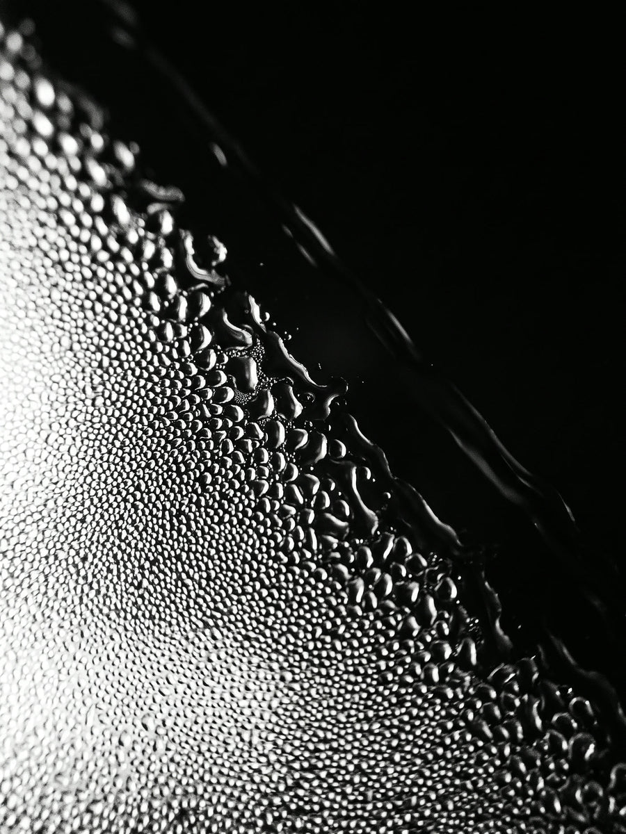 Macro en noir et blanc de gouttelettes de buée qui fusionnent en un film d'eau lisse et transparent