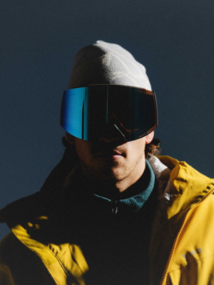 Skieur en tuque blanche et manteau jaune portant la lunette SHIFT à lentille bleue, dans une lumière dure